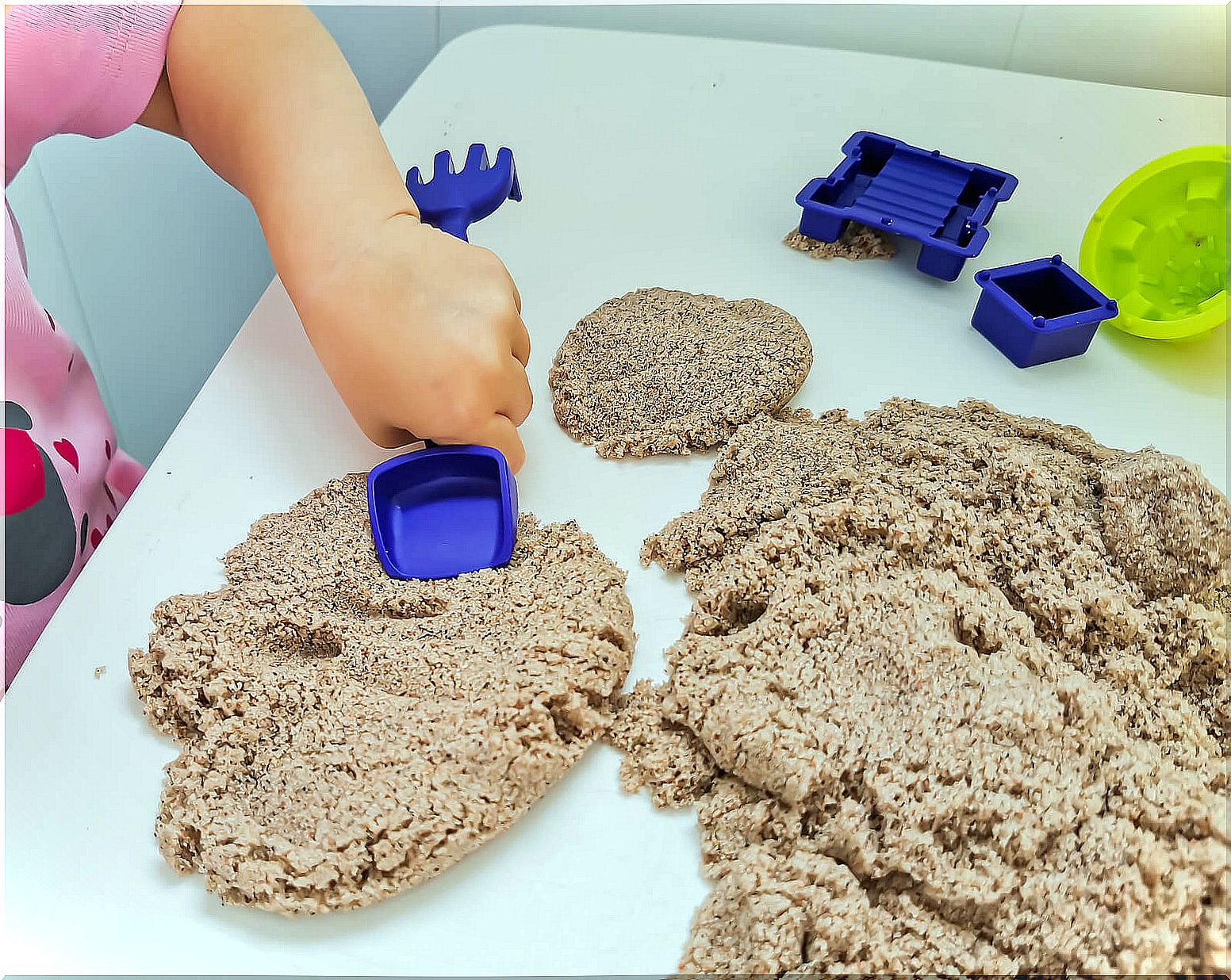 Little girl plays with sand at home.