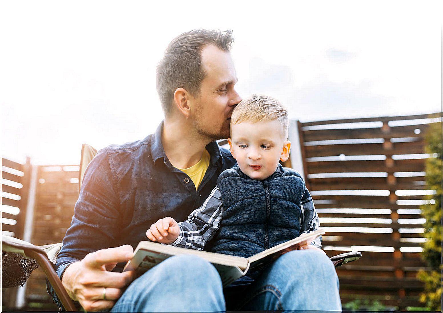 Father giving his son a kiss on the head as they read a book as part of the emotional gift for their education.