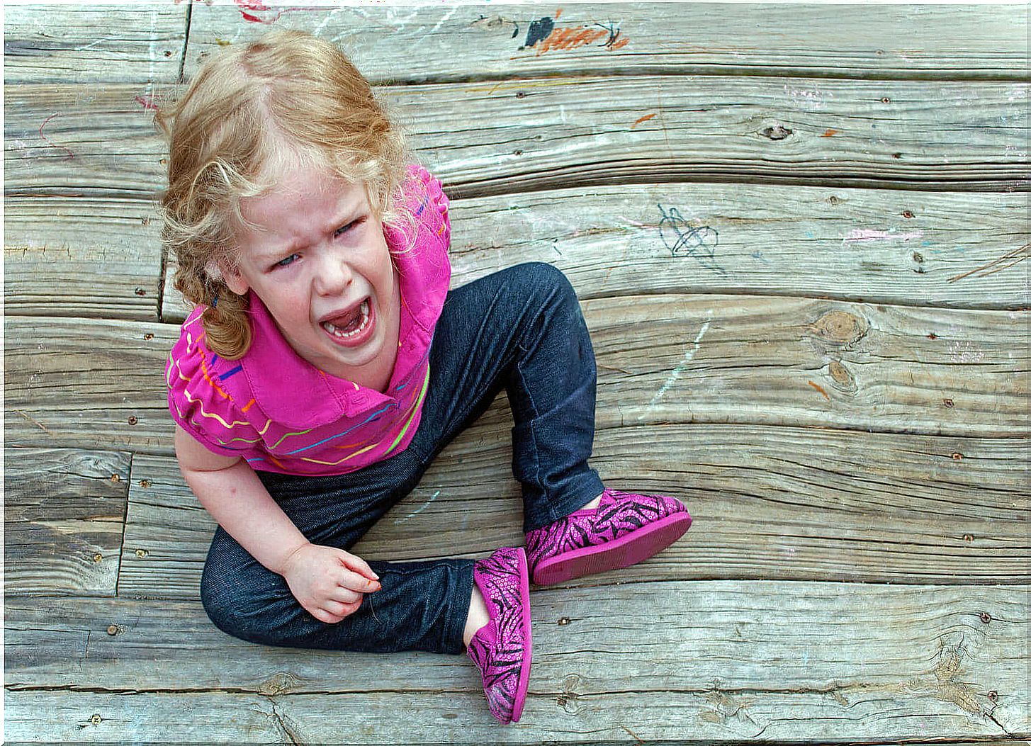 Two-year-old girl sitting on the floor crying out of a tantrum.