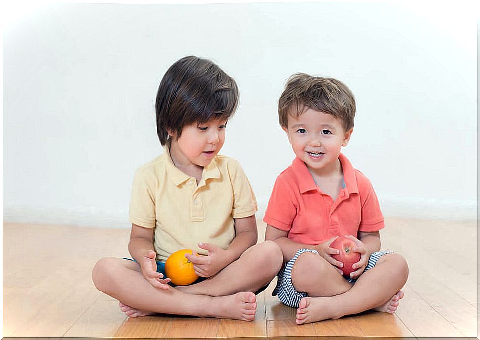 Brothers sitting on the floor with a fruit in hand.